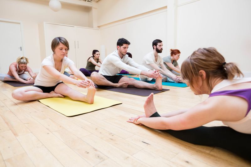 <span  class="uc_style_uc_tiles_grid_image_elementor_uc_items_attribute_title" style="color:#ffffff;">Trainer assisting group of people with stretching exercise in the fitness studio</span>
